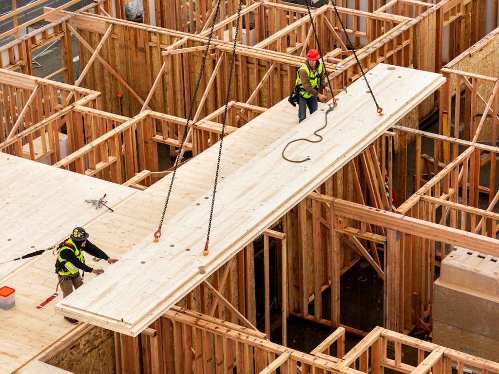 Crane lifting prefabricated panel into timber frame